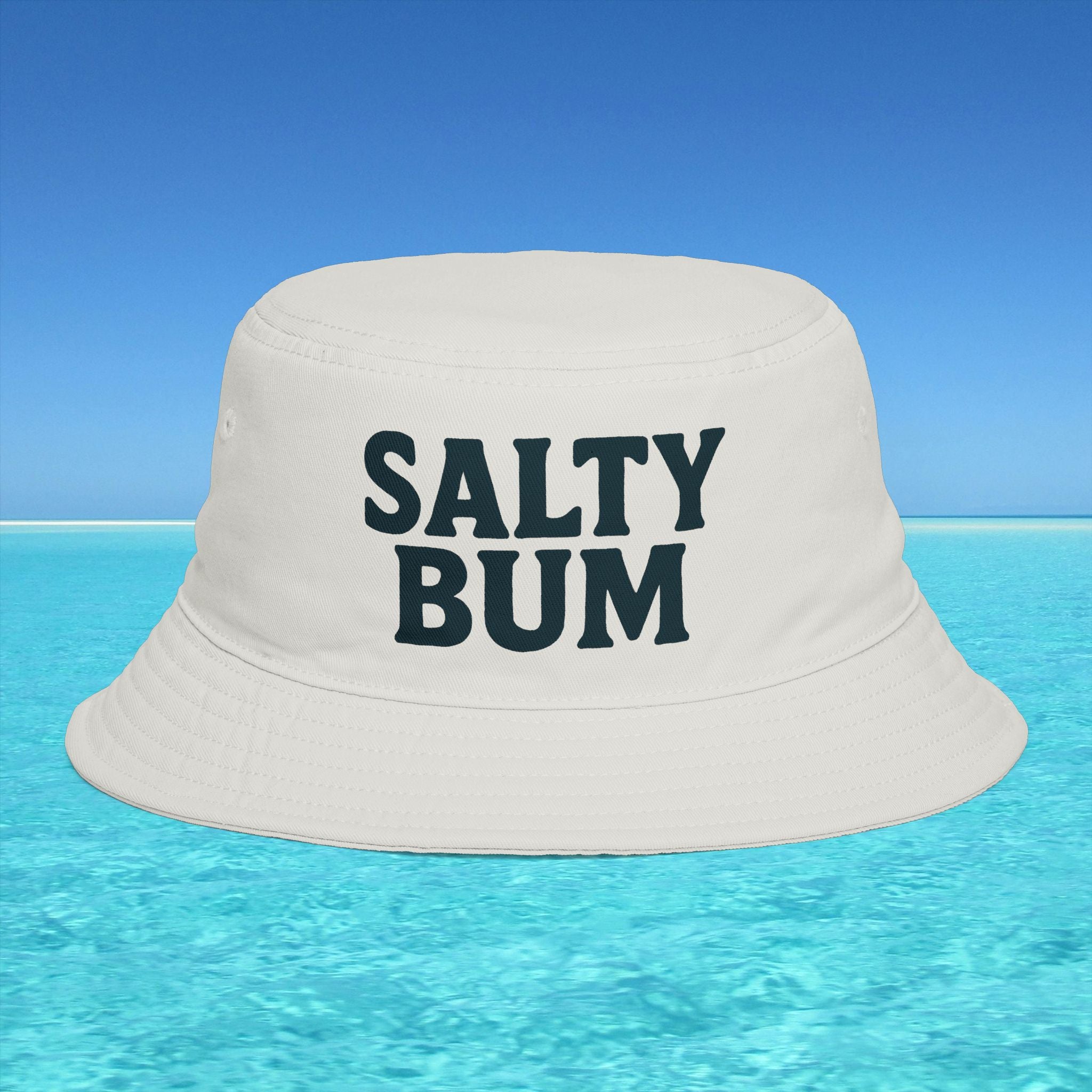 Beige bucket hat with 'Salty Bum' text floating on clear blue water with a blue sky background