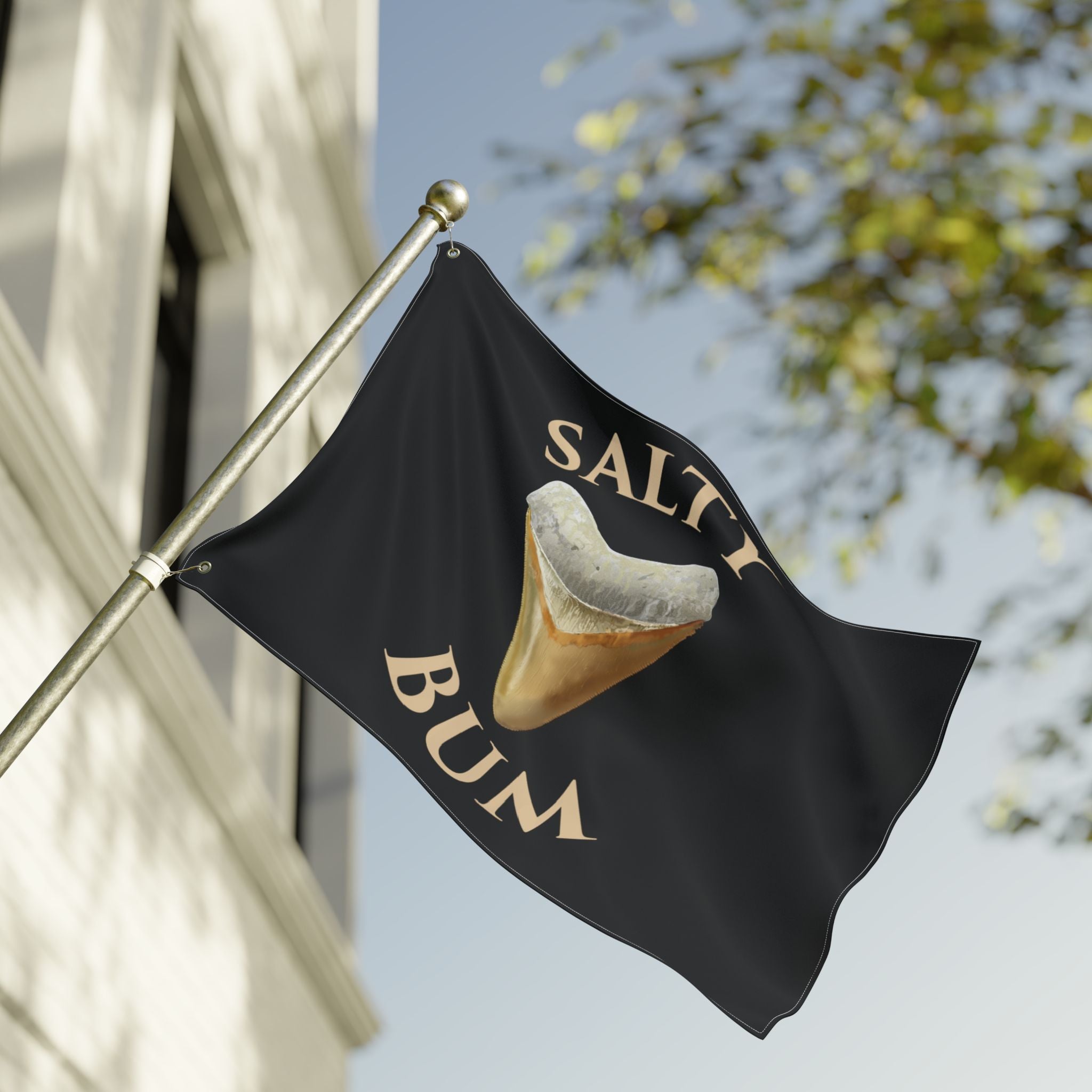 Black flag with a shark tooth graphic and 'Salty Bum' text, waving against a building and tree.