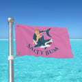 Pink flag with a graphic of a woman on a shark and 'Salty Bum' text, against a clear blue sky.
