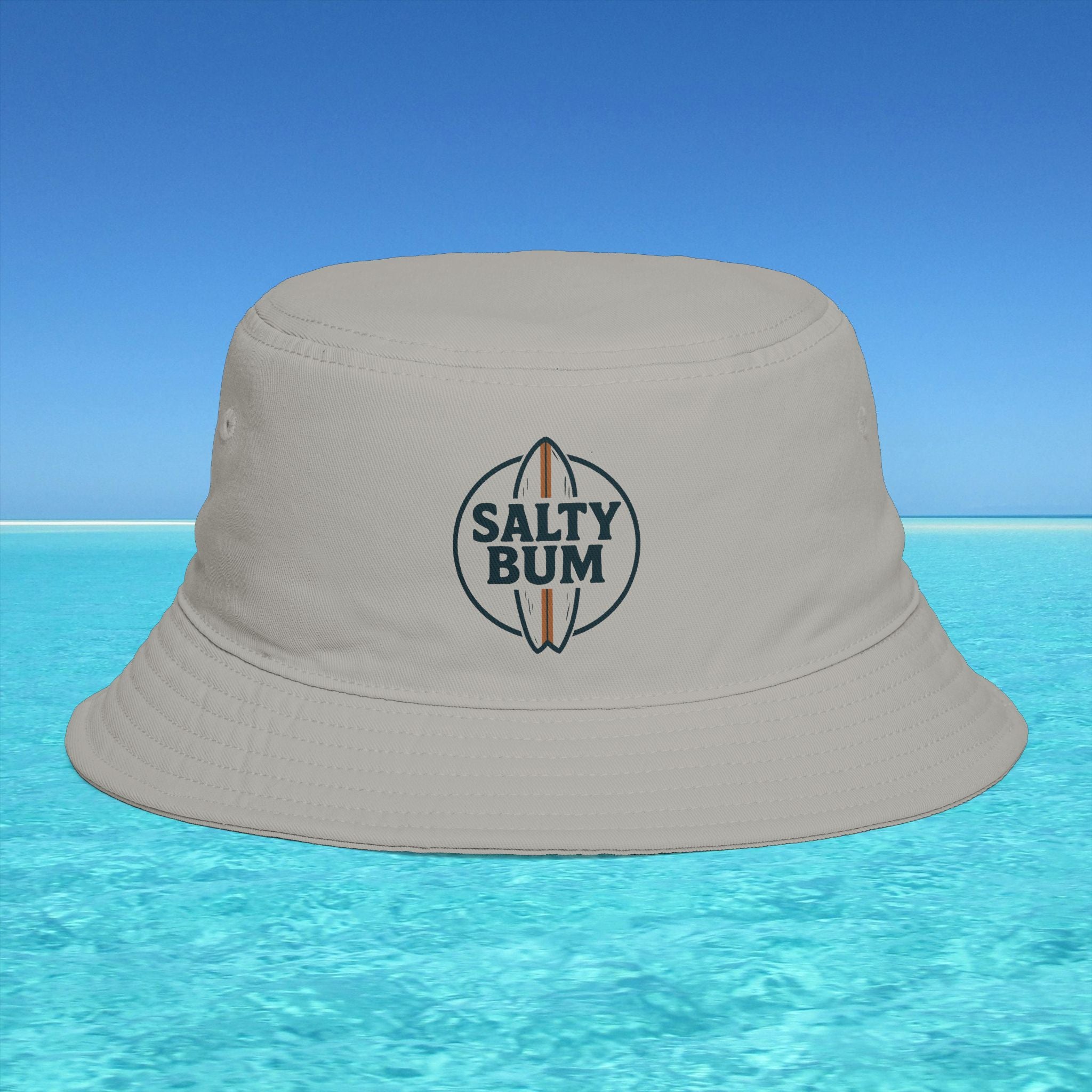 Beige bucket hat with 'Salty Bum' logo on a blue water and sky background