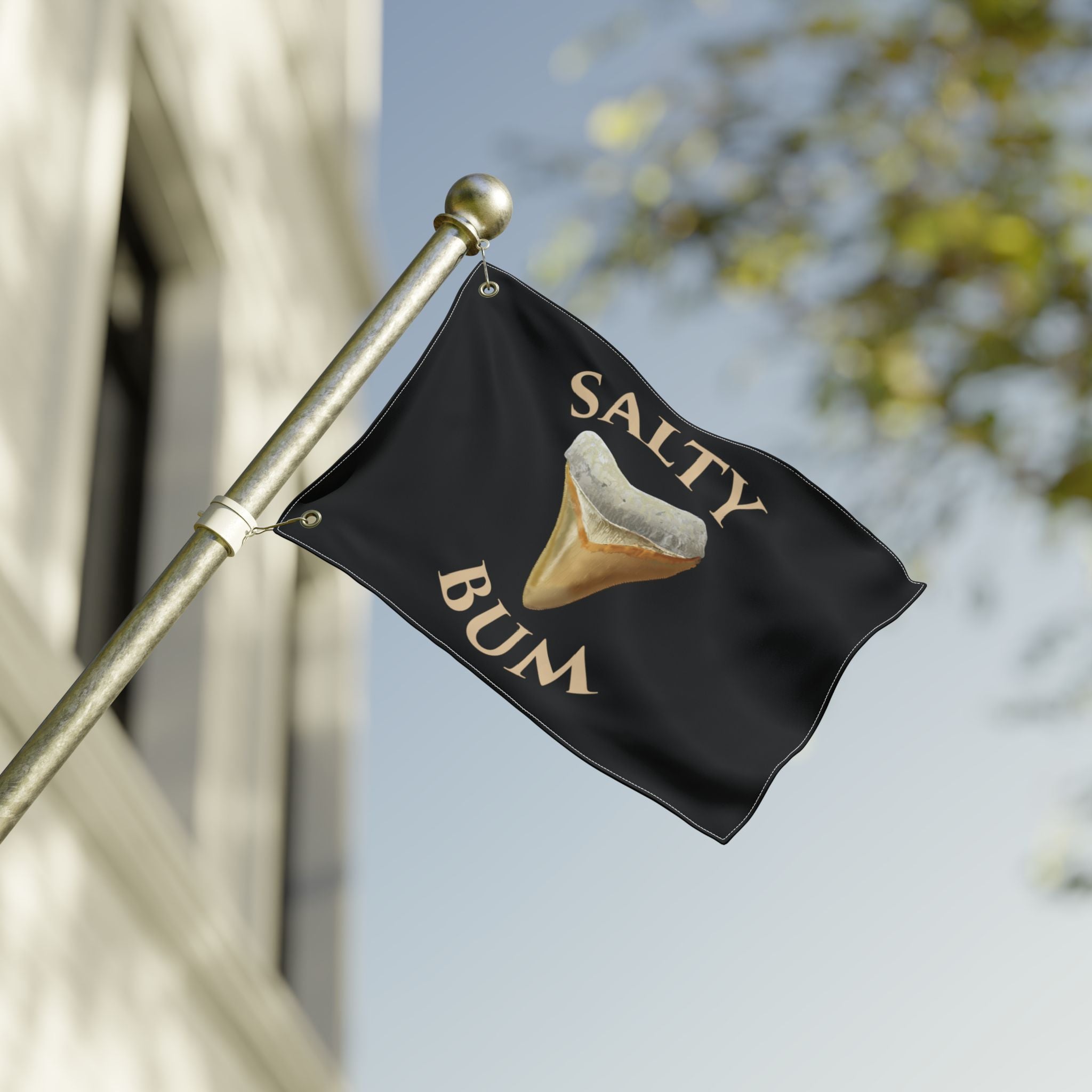 Black flag with 'Salty Bum' text and a sand dollar graphic on a pole against a blurred background.