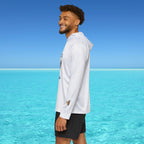 Man standing by clear blue water wearing a white long-sleeve shirt and black shorts.