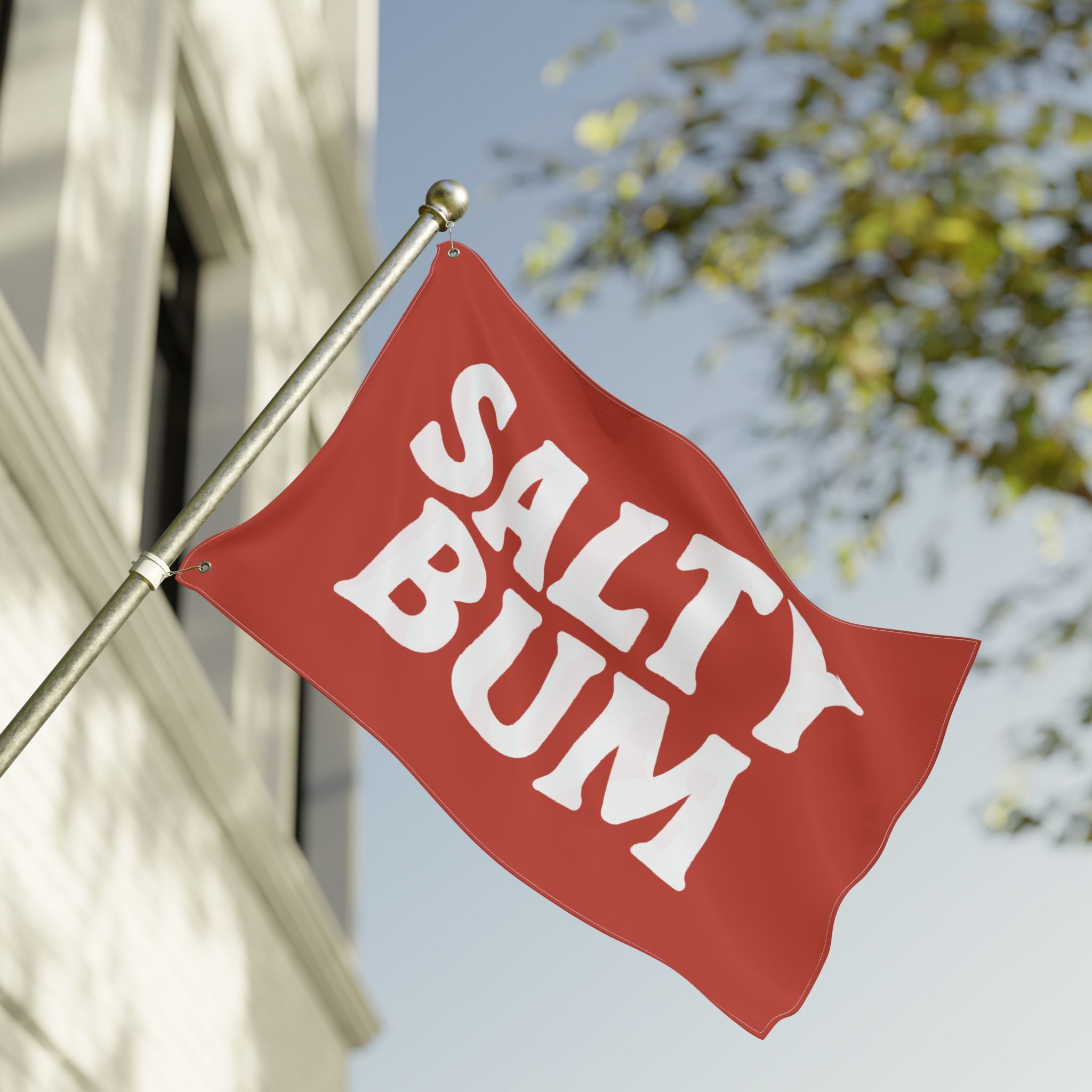 Red flag with 'Salty Bum' text waving in front of a building and tree.
