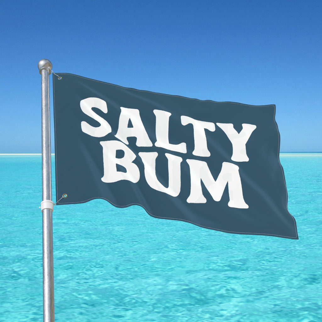 Flag with 'Salty Bum' text waving in front of a clear blue sky and ocean.