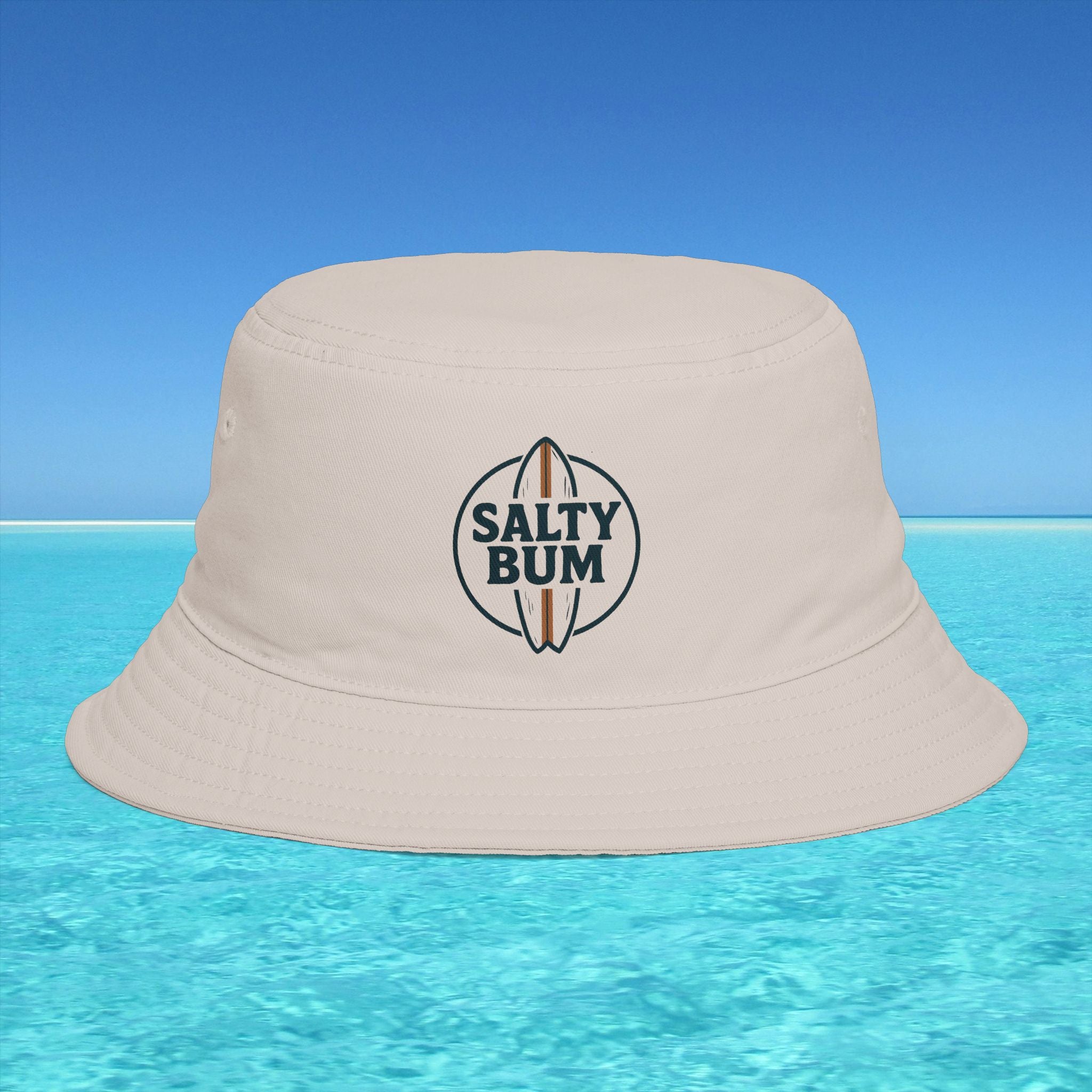 Beige bucket hat with 'Salty Bum' logo on a blue water and sky background