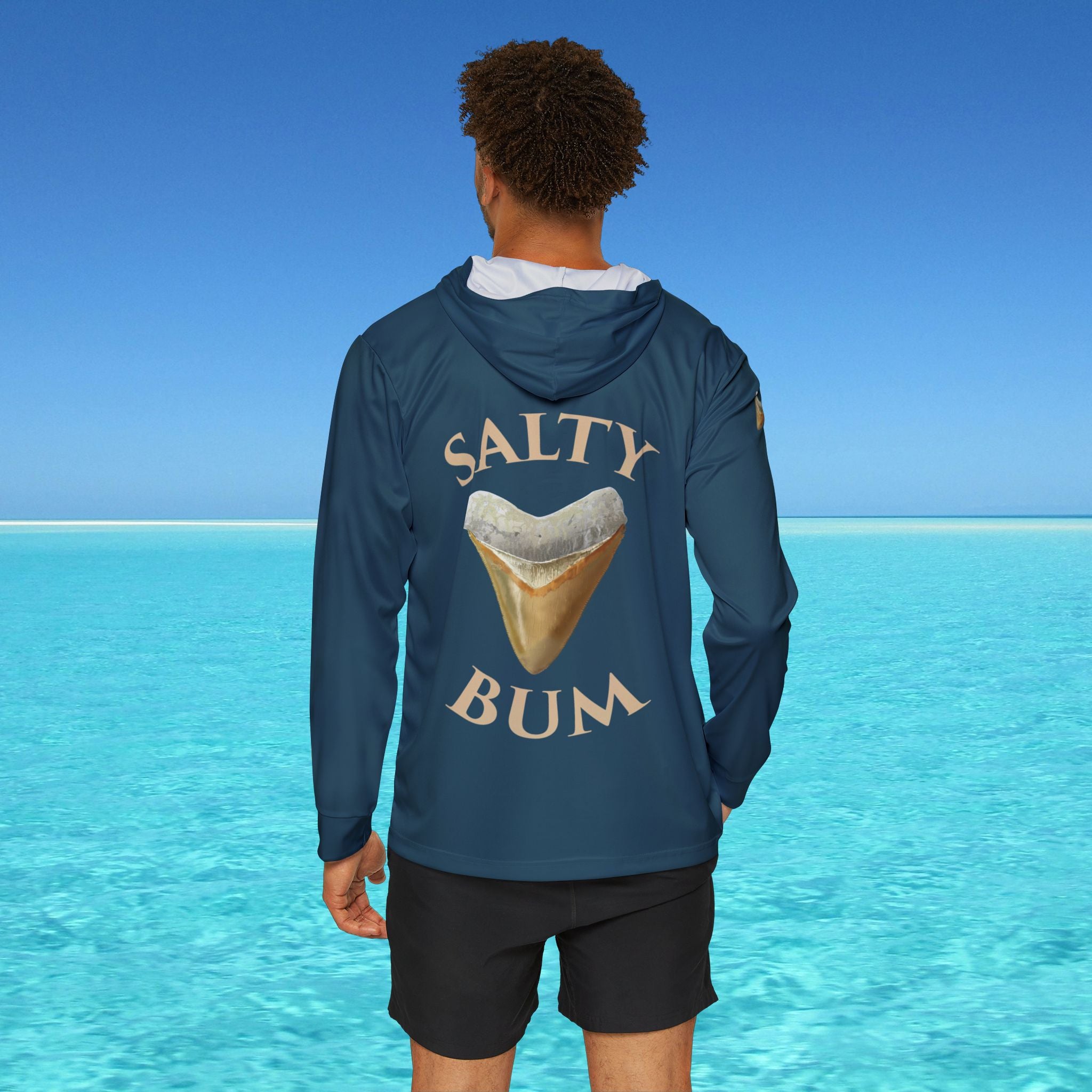 Person wearing a blue hoodie with 'Salty Bum' text and shark tooth graphic against a clear blue sky and ocean.