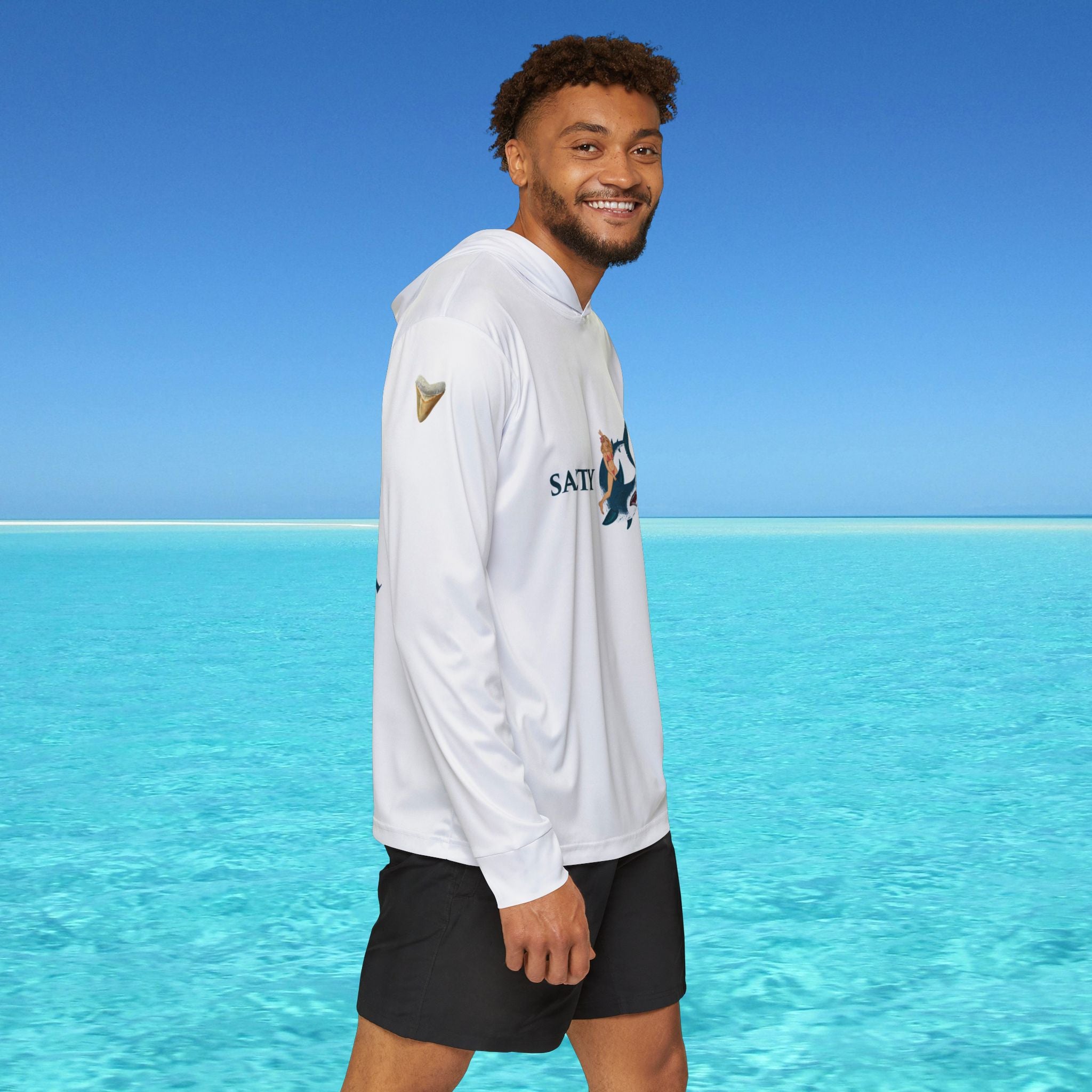 Man wearing a white hoodie with a logo standing in front of clear blue water and sky.