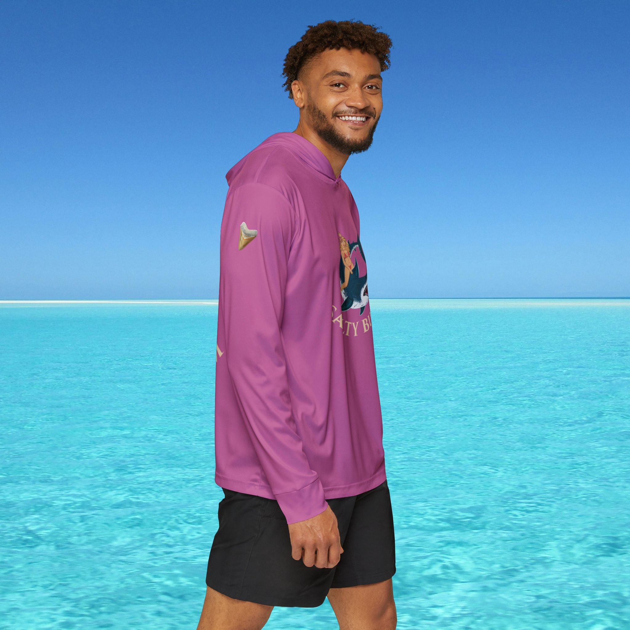 Man wearing a purple hoodie with a graphic design standing in front of clear blue water and sky.