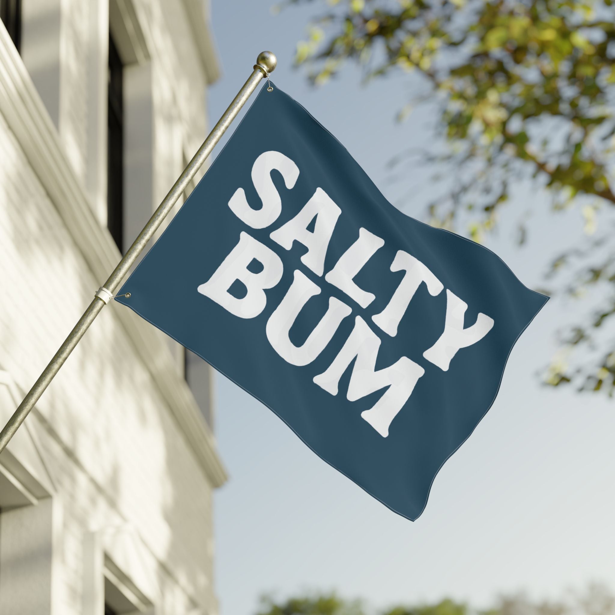 Flag with 'Salty Bum' text waving in front of a building and tree.