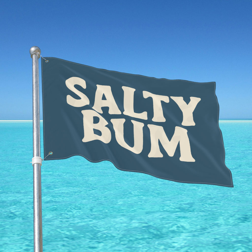 Flag with 'Salty Bum' text waving in front of a clear blue sky and ocean.