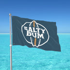 Flag with 'Salty Bum' logo waving in front of a clear blue sky and ocean.