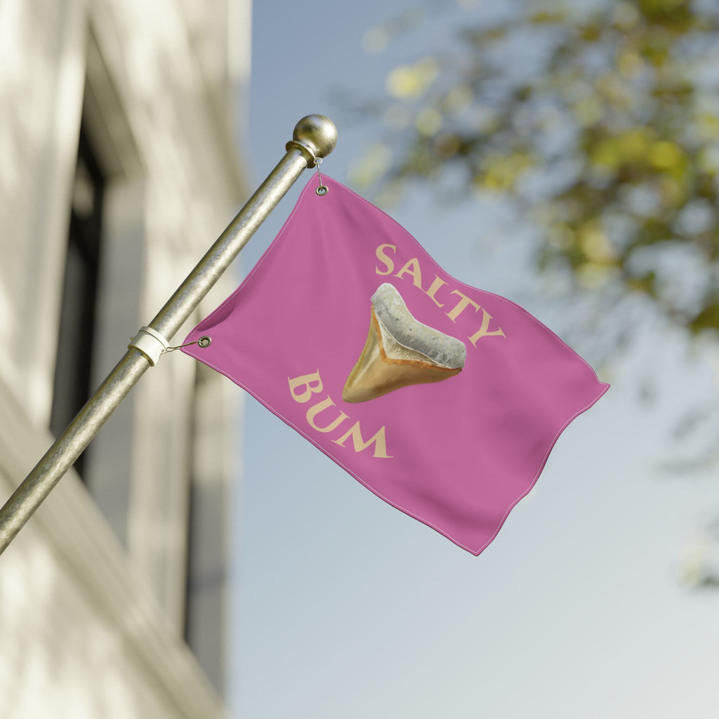 Pink flag with 'Salty Bum' text and shark tooth graphic on a pole against a blurred background