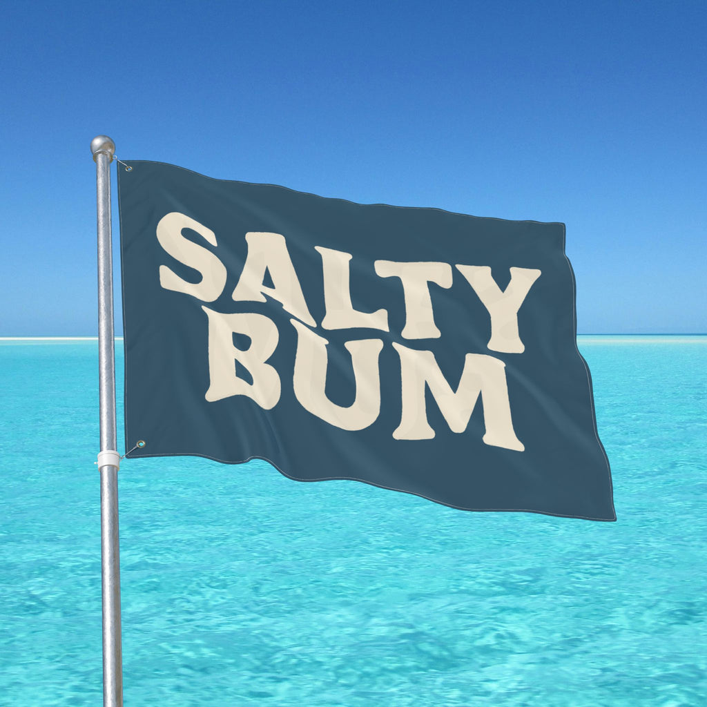 Flag with 'Salty Bum' text waving in front of a clear blue sky and ocean.