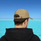 Person wearing a beige cap and black hoodie with a blue water and sky background