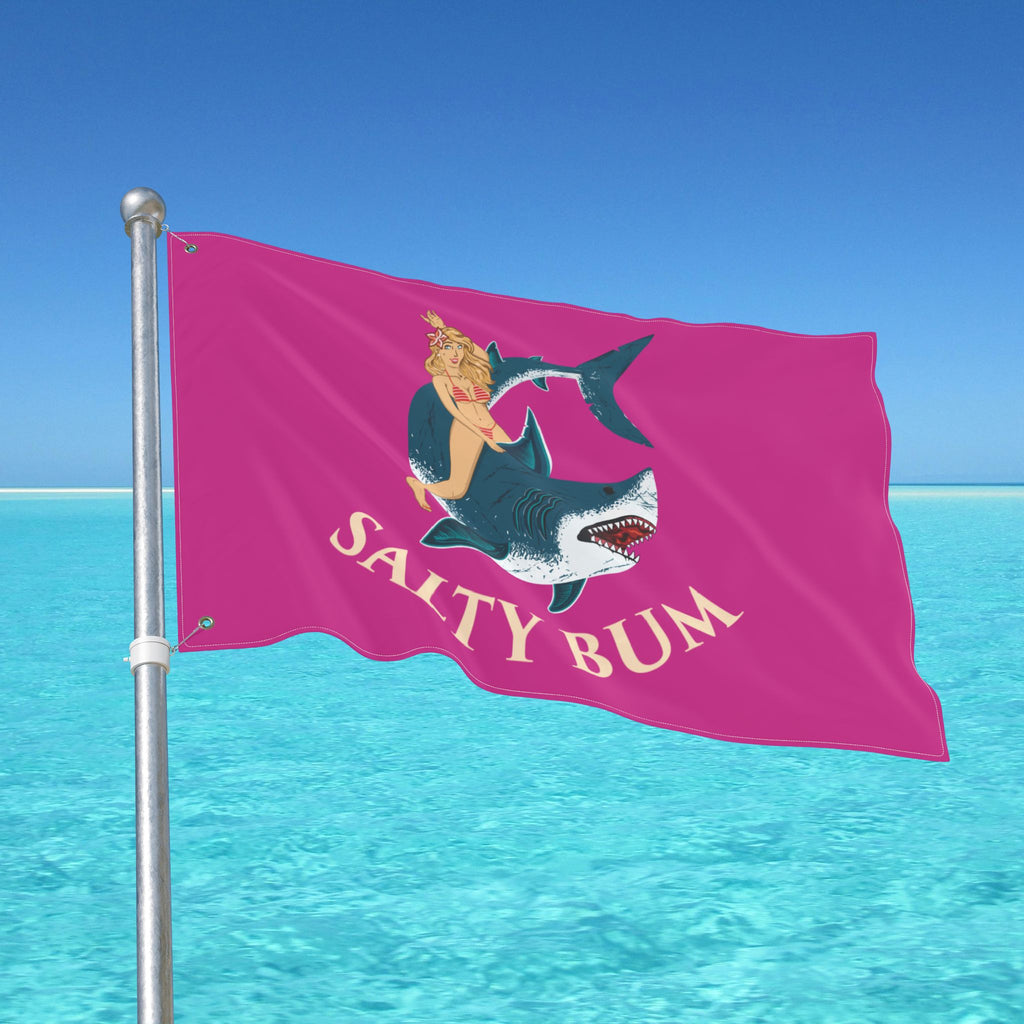 Flag with 'Salty Bum' design on a pole against a blue sky and ocean background