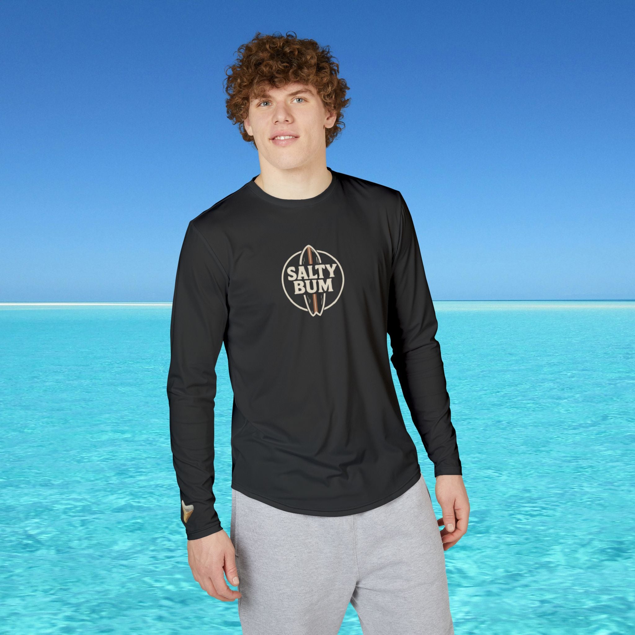 Person wearing a black long-sleeve shirt with 'Salty Bum' logo against a clear blue sky and ocean background