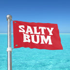 Red flag with 'Salty Bum' text against a clear blue sky and ocean.