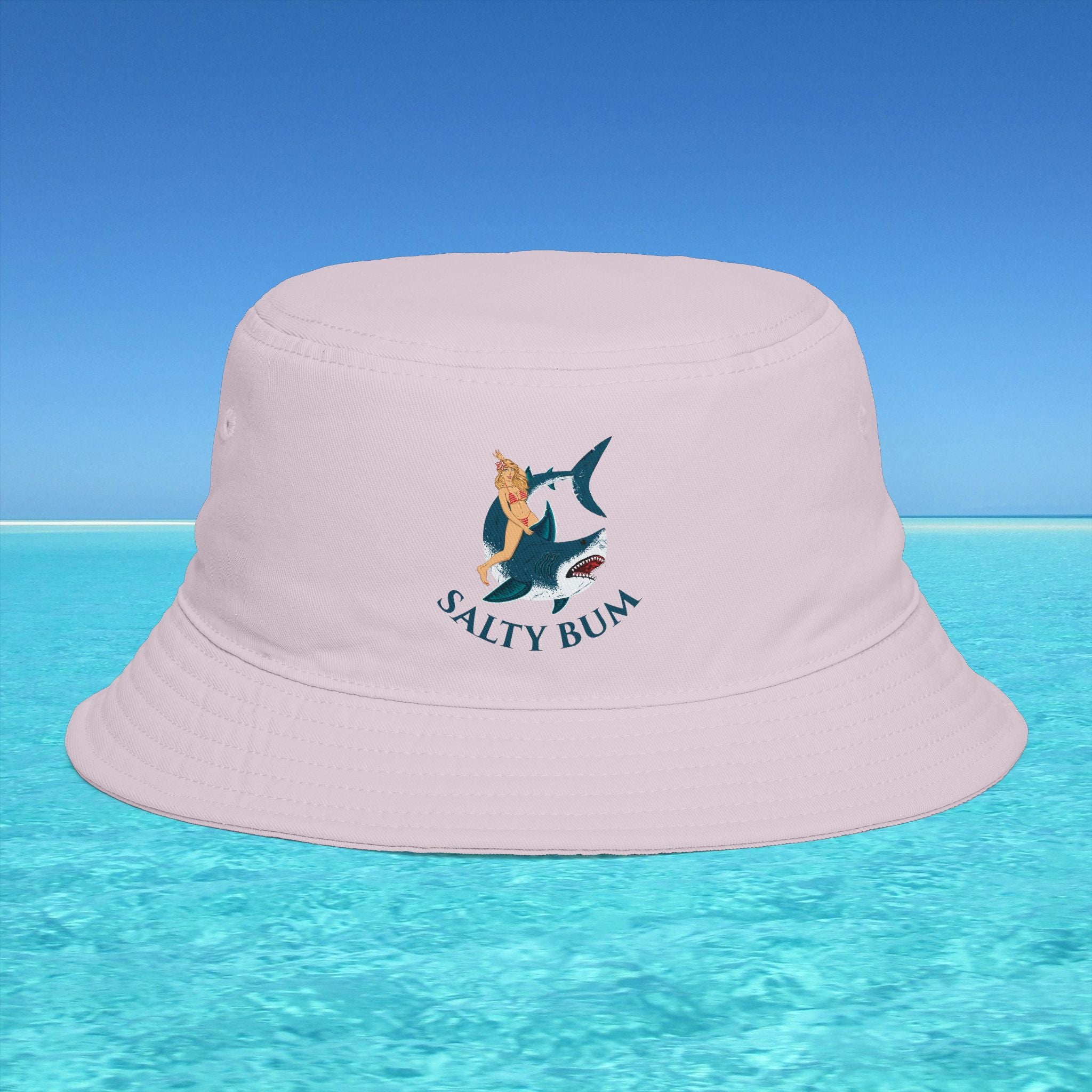 Pink bucket hat with 'Salty Bum' logo on a clear blue water and sky background
