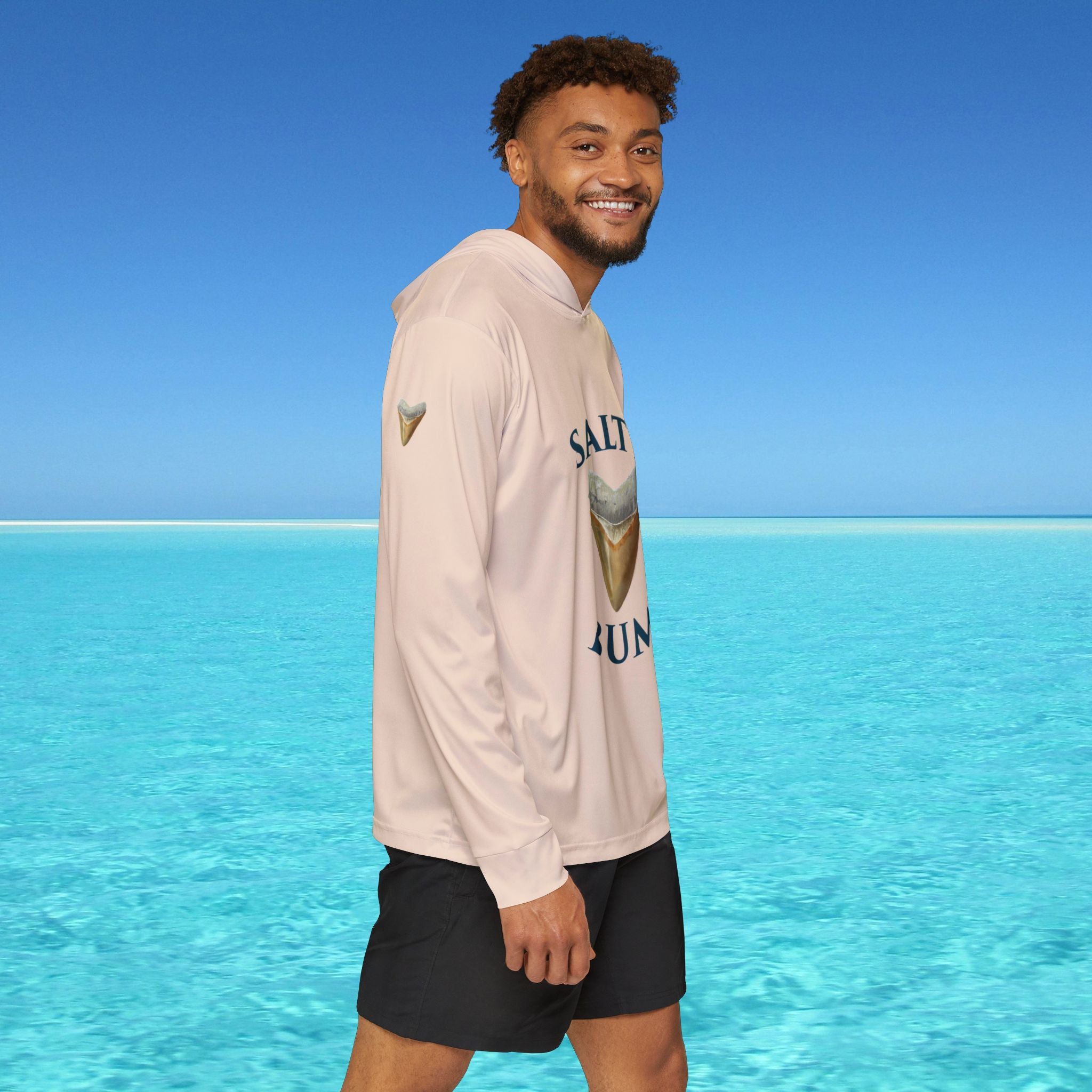 Man wearing a hoodie with ice cream cone design and text standing in front of clear blue water and sky.